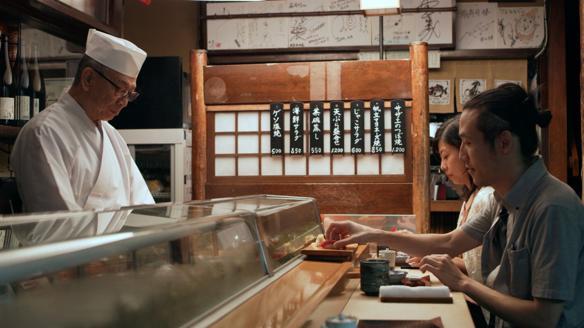 Un itamae prepara sushi tras la barra mientras dos clientes comen frente a él