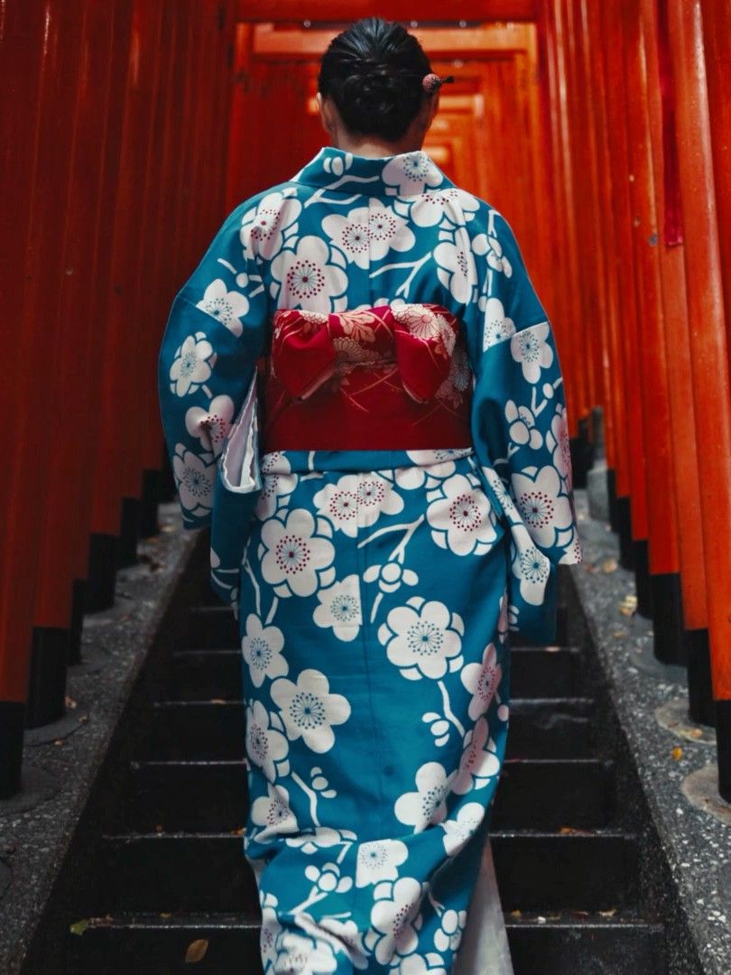 Una mujer en kimono sube una escalera por un túnel de toriis rojos